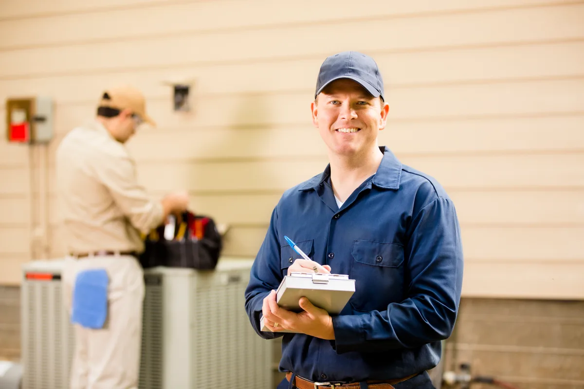 Two technicians performing scheduled maintenance on a home air conditioning unit
