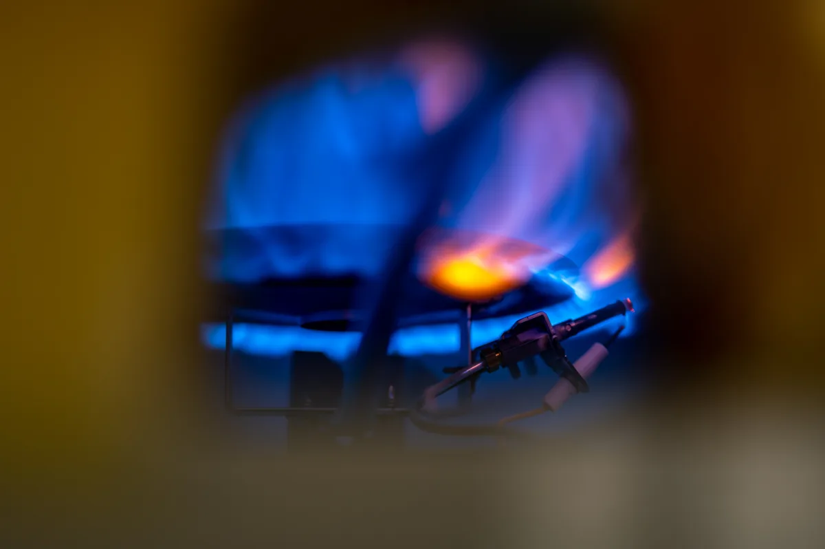 Small blue pilot flame burning inside the burner compartment of a gas water heater