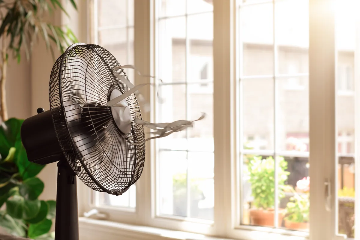 Upstairs bedroom on a hot summer afternoon with a portable fan running beside the bed