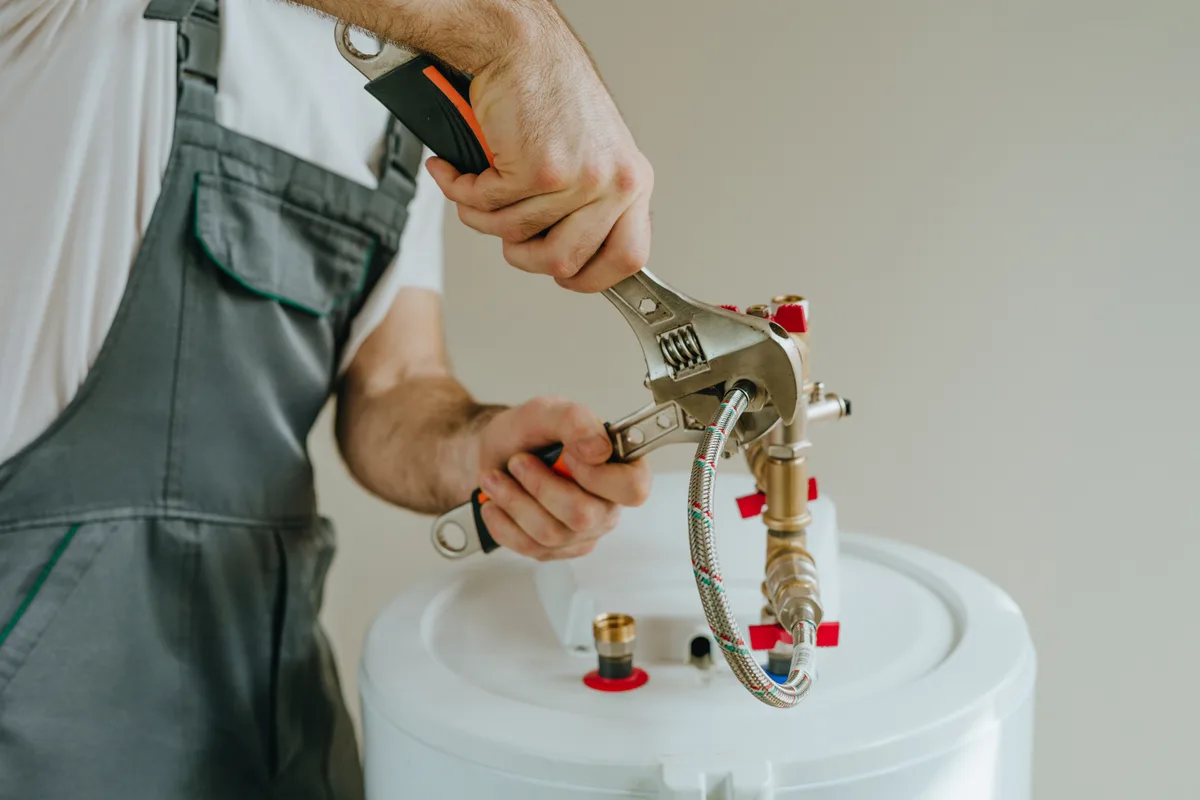 Technician repairing a residential water heater with a wrench