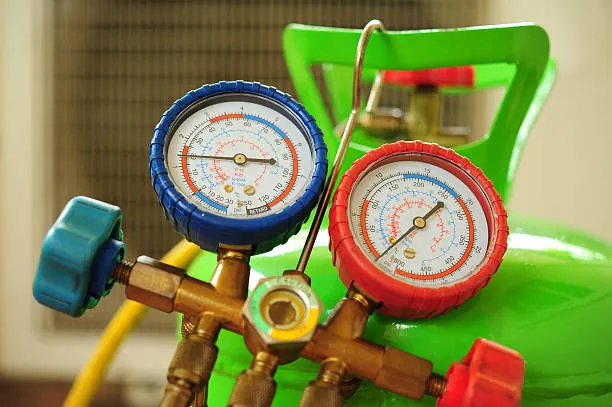 AC technician using manifold pressure gauges on rooftop unit