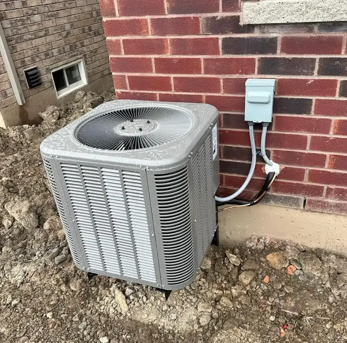 Residential AC condenser unit installed beside brick exterior