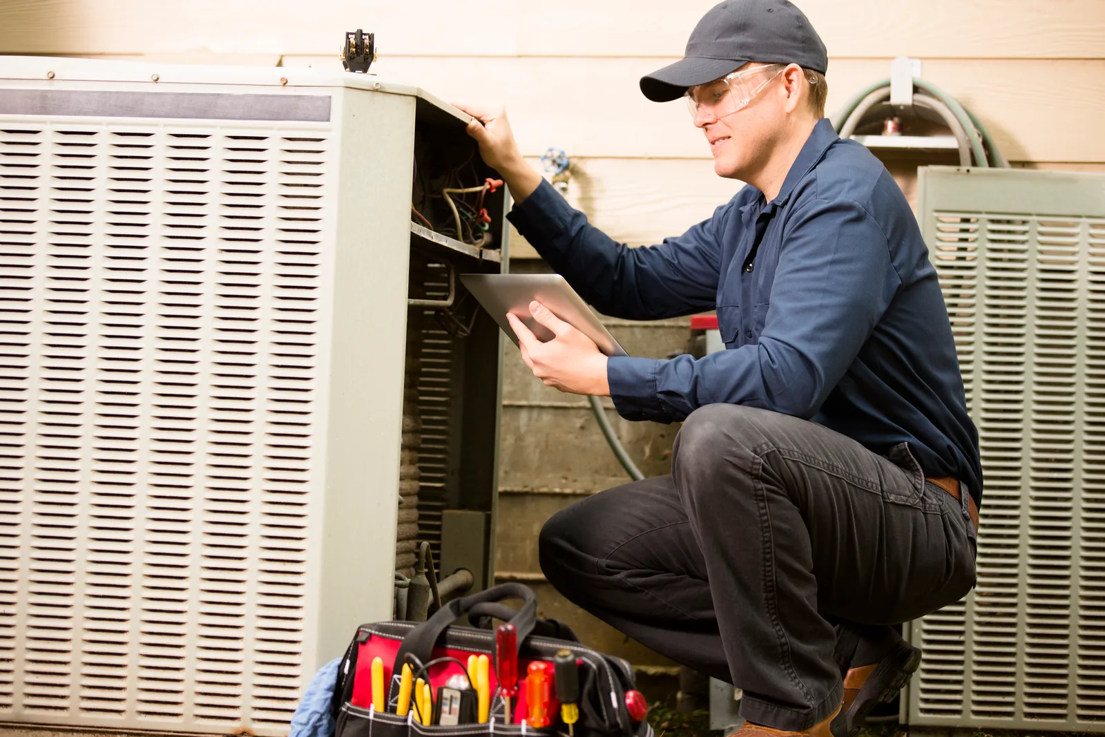 HVAC technician diagnosing an outdoor AC condenser with a tablet