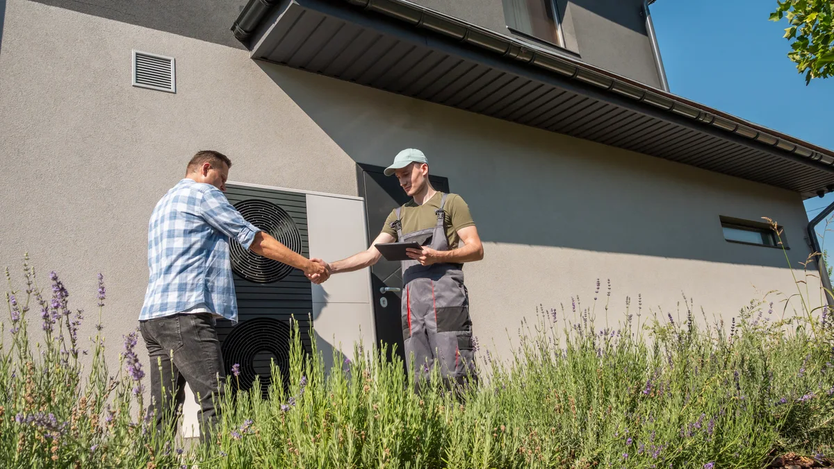 Homeowner and technician shaking hands beside an outdoor heat pump unit
